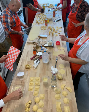 Group of people in red aprons make ravioli on a long wooden butcherblock counter